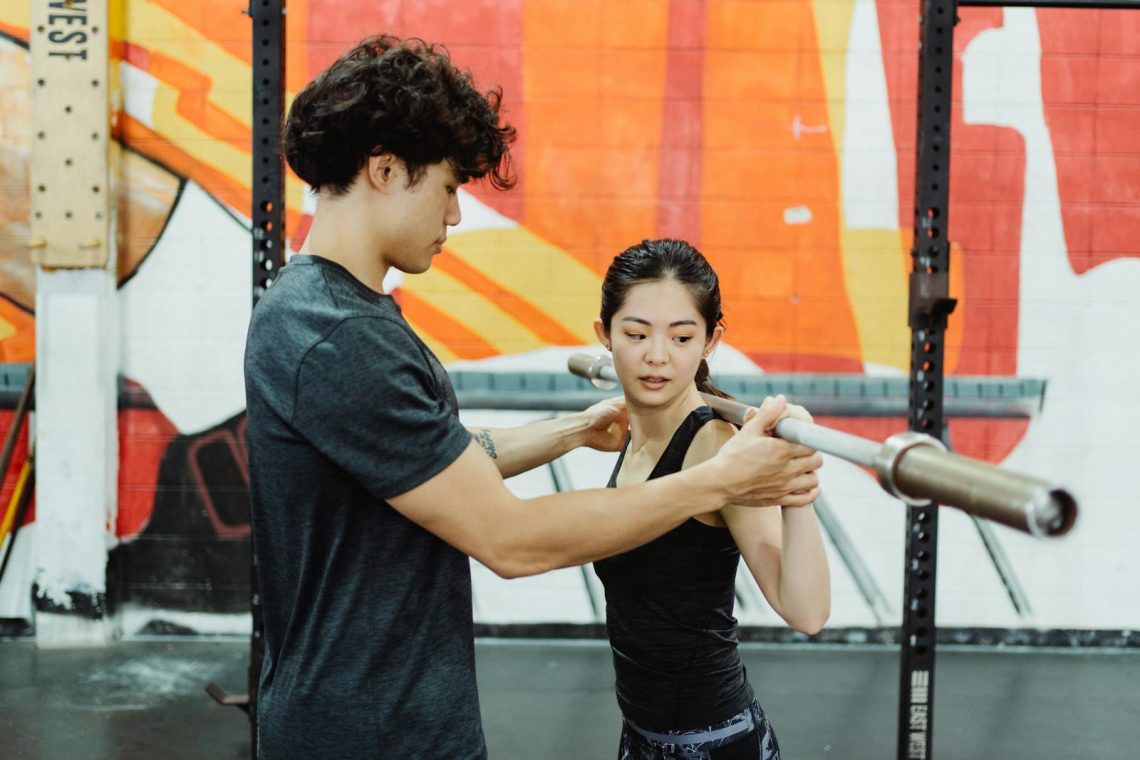 A personal trainer guides a woman lifting a barbell indoors, focusing on technique and strength training.