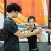 A personal trainer guides a woman lifting a barbell indoors, focusing on technique and strength training.